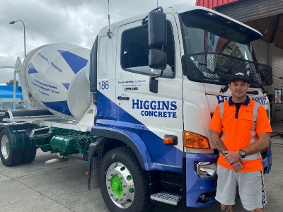 Ryan Pickering wearing a hi-vis shirt standing in front of a blue and white eight tonne Higgins concrete truck.