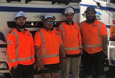 Four mean in hard hats and high visibility clothing in front of a truck.