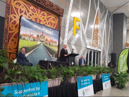 Rotorua Mayor Steve Chadwick standing on a podium with two men sitting on stage.