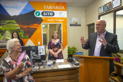 A man at a podium animatedly speaking while three people look on smiling.