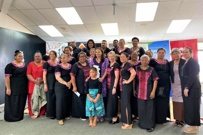 A group of smiling people standing together for the photo. A few are wearing matching black and purple Pacific wear.