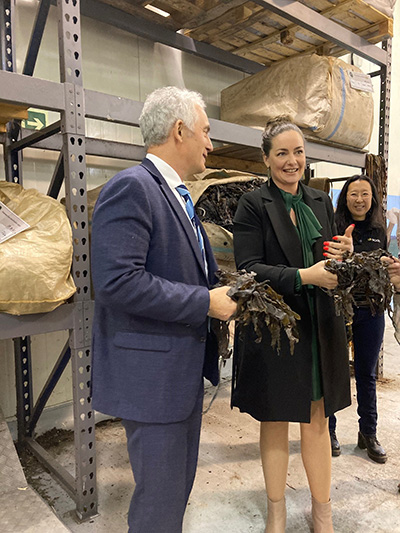 Minister Nash and AgriSea Chief Executive Clare Bradley standing in a manufacturing warehouse holding seaweed