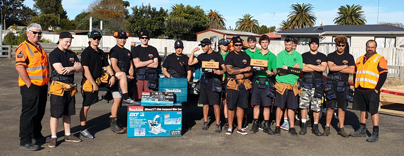 A group of students and Mitre10 staff stand in front of donated tools.