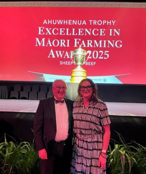 Robert Pigou and Charlotte Severne stand together in front of a red sign that features a gold trophy.