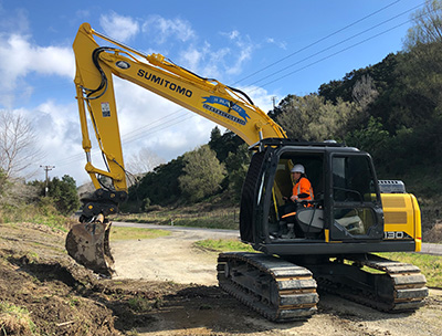 Te Rangi Marie Bartlett using a digger on a work site next to a road.