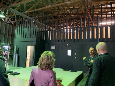 In a warehouse-like film studio building, a person is showing a couple of people around.