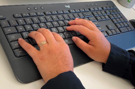 A pair of hands at work on a dark grey computer keyboard.