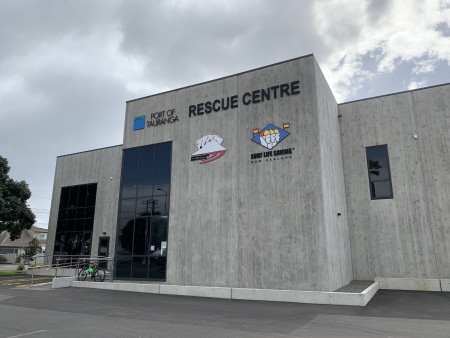 A new, grey building with tall, tinted windows, a flat roof and sponsorship logos on it