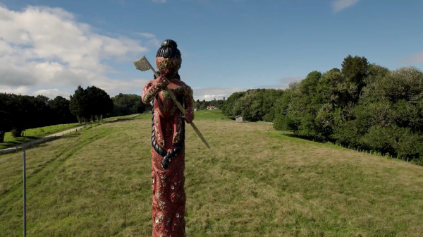 A wooden post carved with Māori designs standing tall in a green grass field