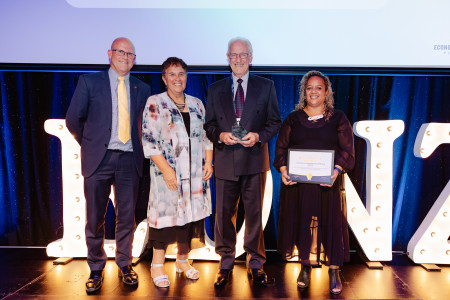 4 people standing on stage, smiling and holding up a certificate and the Inclusive Well Being Award