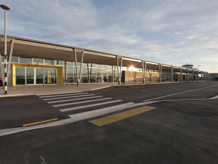 The outside of the Invercargill Airport showing the main entrance, pedestrian crossing and the sun reflecting off the glass panels on the side of the building.