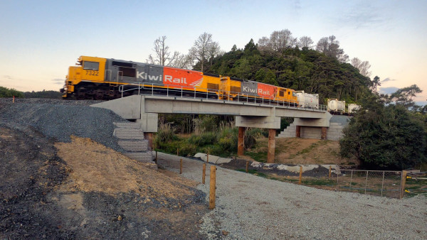 Low angle shot of a KiwiRail train going across a small bridge with piles of gravel beneath it
