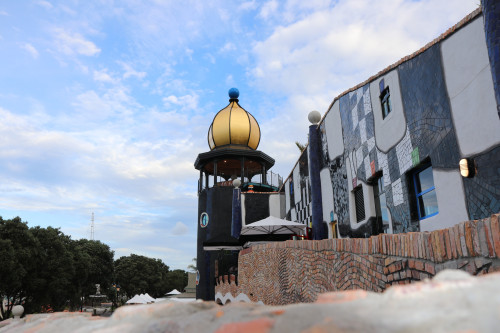 A modern building with grey and white checkered pattern on the exterior walls, a brick wall in front and a round black building with a yellow dome roof