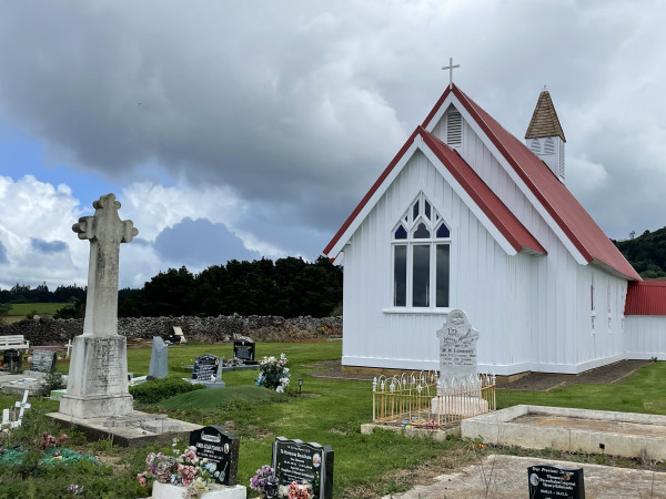 A white church building with a red roof, with headstones on the grass surrounding the building