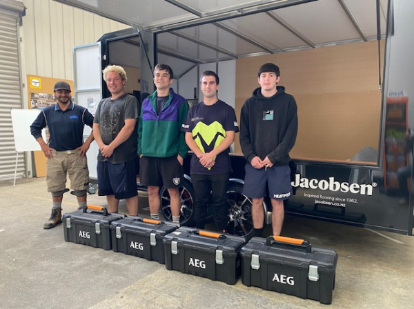 Five young men standing in front of a trailer and behind tool boxes