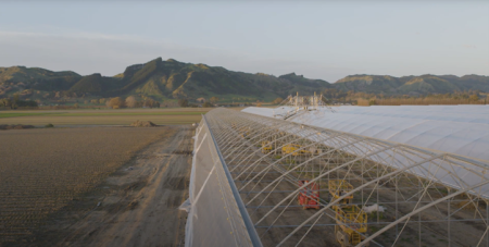 High angle image of a large clear gazebo with machinery inside it, on an open area of land, with green hills in the distance