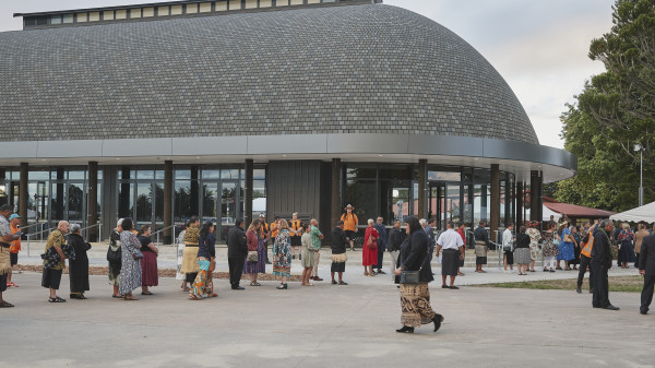 A new building with a rounded brick roof, with people in traditional Pasifika clothing gathering outside it