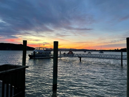 A boat the end of a wharf with hills and a pink and orange sunset in the background.