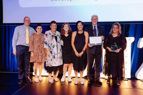  7 people standing on stage, smiling and holding up a certificate and the Overall Supreme Award