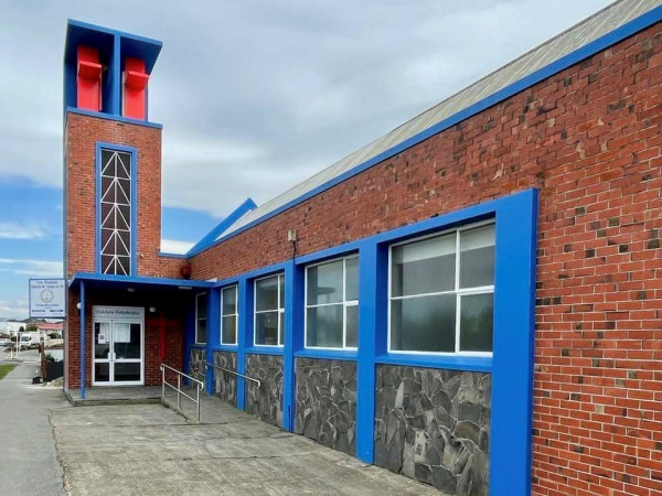 A brick building with blue trim around the windows. It is a long building with a tall square point on one end