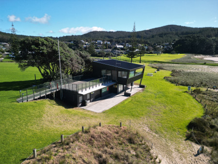 A new, two storey black building with wrap around windows and a balcony, looks over grass and sand dunes